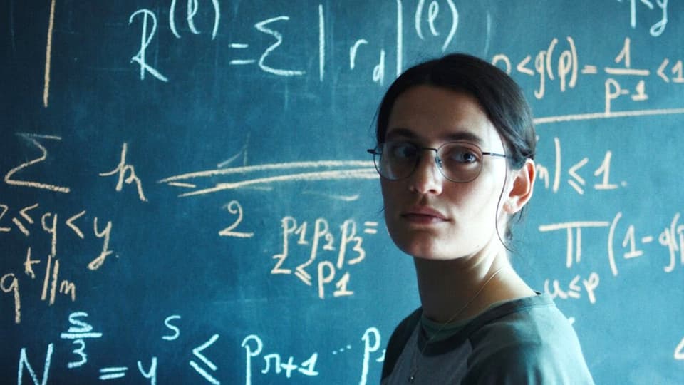 A young woman in front of a blackboard full of mathematical formulas.