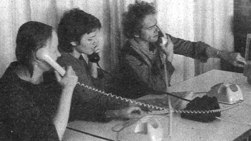 Black and white photo with two women and a man sitting next to each other and talking on the phone.