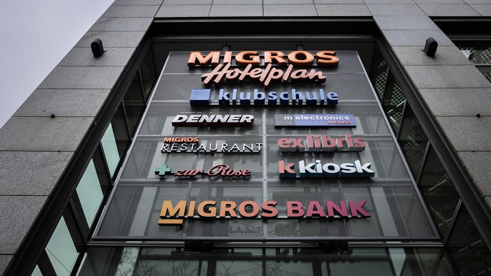 Logos of many Migros subsidiaries on a building.  These include Hotelplan and Migros Bank