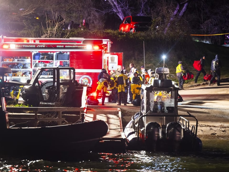 Photo taken at night, water and boats in the front, rescue vehicles and people in firefighting gear in the back