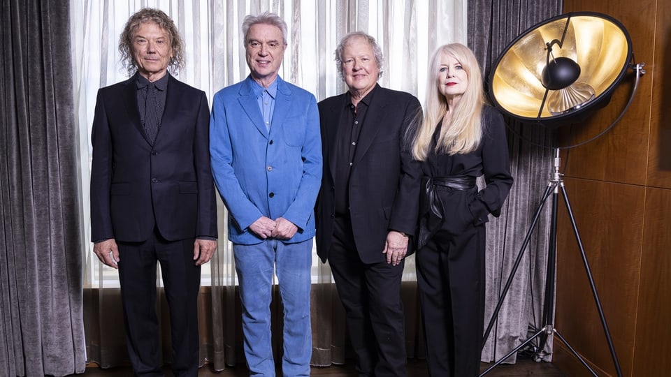 The four members of the band “Talking Heads” were photographed in formal clothing in front of a closed curtain in 2023.