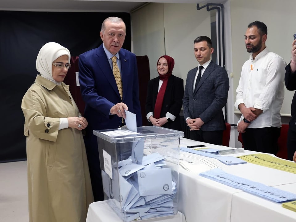 Recep Tayyip Erdogan stands with his wife at a polling station and throws a letter into an urn.