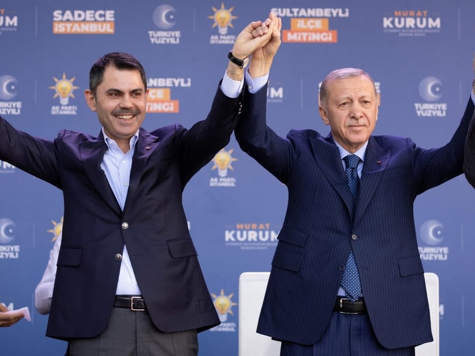 Erdogan and Kurum stand together on a stage and hold their hands in the air.