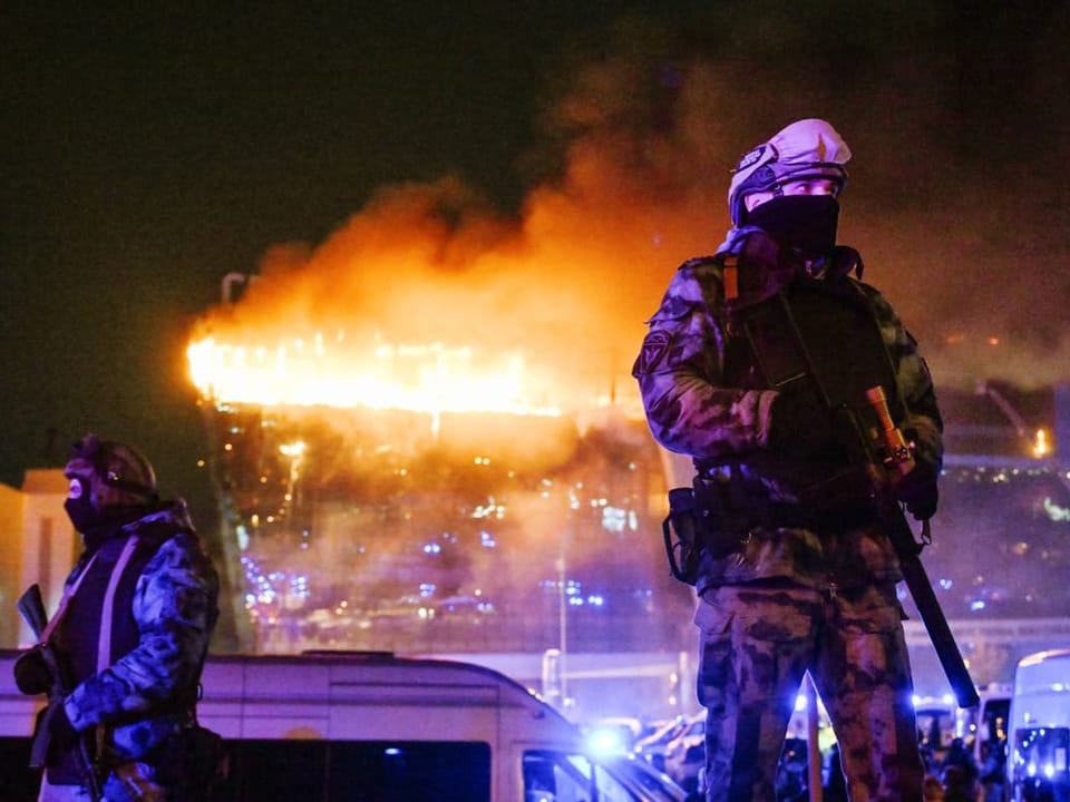 Security forces in front of a burning building.