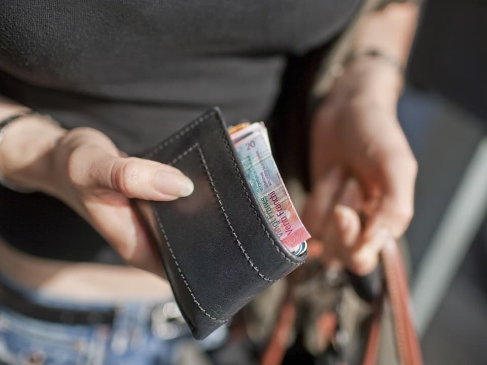 A woman holds a wallet in her hand.  The edge of a 20 franc note can be seen.