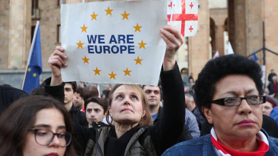 People protest in Tbilisi.  A woman holds up a poster with “we are Europe”.