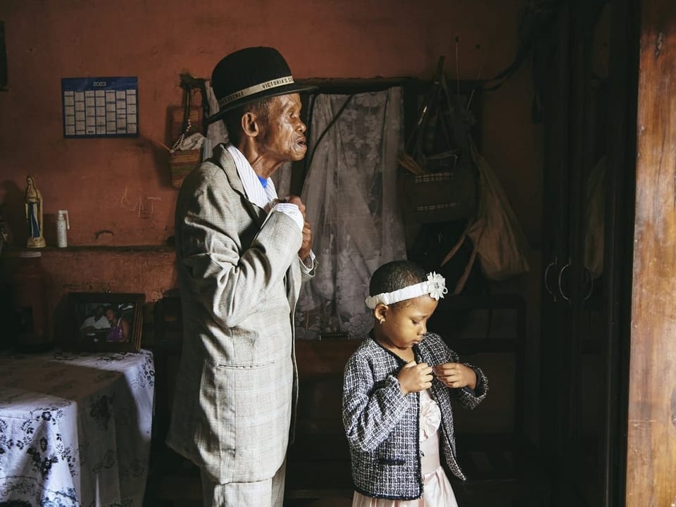 Old man and child, both getting dressed with jackets, oriented to the right in the picture