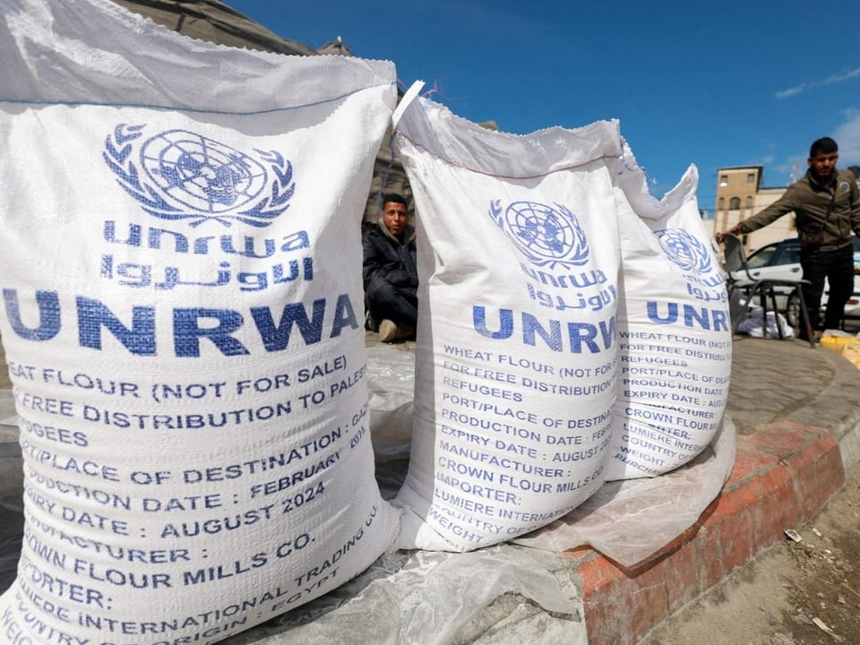 Picking up bags of flour.  They are labeled UNRWA.  Men stand and sit next to them.