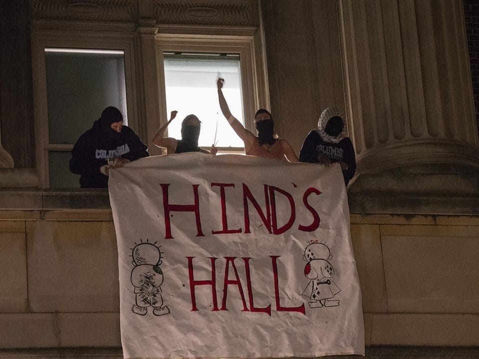 People wearing masks hold a banner reading 'HINDS HALL' on a building.