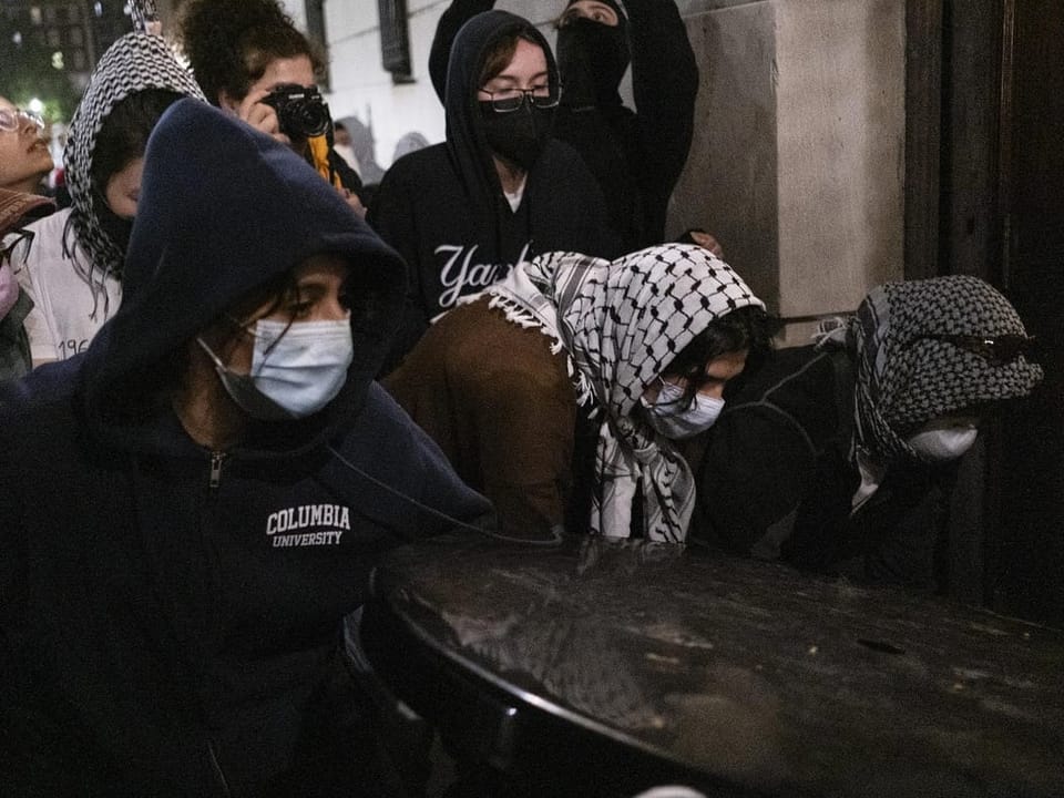 People in hoods and masks at a nighttime gathering on the street.