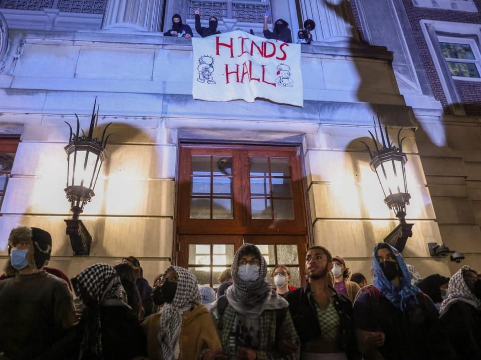 Protesters wearing face masks and headscarves outside Hinds Hall at night.