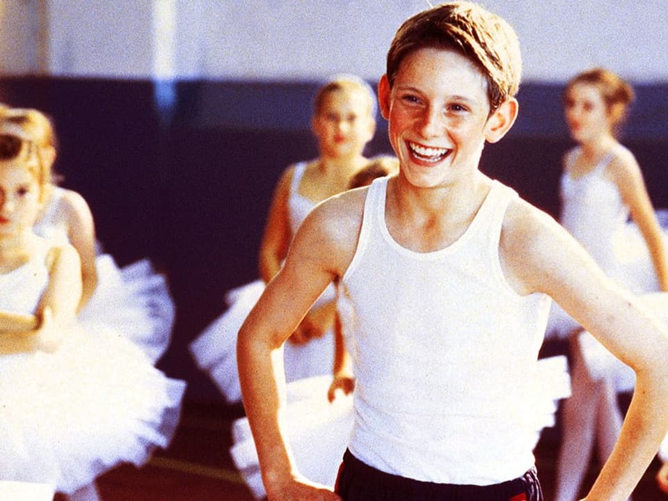 A little boy stands in the middle of young ballerinas